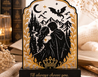 May include: An arched decorative display featuring a black silhouette of a couple, a castle, mountains, and a dragon against a white background. The frame is adorned with gold leaf-like patterns and a crown. The black base reads, I'll always choose you.