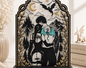 May include: A decorative arched wooden display featuring a black silhouette of two figures embracing, with a teal dragon tattoo on the back of one figure. The background shows mountains, trees, a crescent moon, and stars. The base reads In my Romantasy Era.