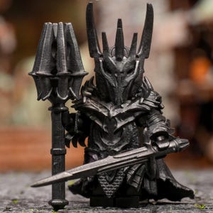 以下が含まれることがあります： 剣と槍を持った黒い鎧姿のキャラクターのフィギュア。フィギュアは、高く尖った特徴を持つヘルメットをかぶっています。鎧には複雑なディテールがあり、流れるようなマントが付いています。