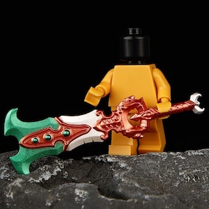 Puede incluir: Una minifigura de Lego sosteniendo una espada decorativa. La espada presenta una hoja verde, un centro blanco y detalles en rojo y dorado. La minifigura es amarilla con una cabeza negra.