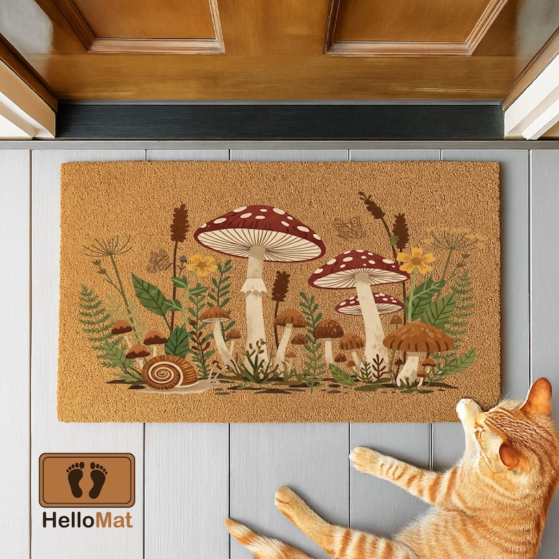 Puede incluir: Una alfombra rectangular con un dise&ntilde;o de setas. La alfombra presenta grandes setas rojas y blancas, setas marrones m&aacute;s peque&ntilde;as y varias plantas y flores. El texto "HelloMat" es visible en la parte inferior izquierda.