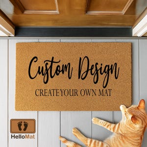 May include: A rectangular doormat with the words "Custom Design" and "CREATE YOUR OWN MAT" in black script. The mat is a light brown color and has a textured surface. A logo for HelloMat is in the lower left corner. An orange tabby cat is lying on the floor.
