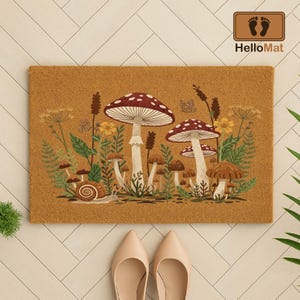 Puede incluir: Una alfombra rectangular con una ilustraci&oacute;n detallada de setas, plantas y un caracol. Las setas tienen sombreros rojos y blancos con lunares. La alfombra es marr&oacute;n con el texto "HelloMat".