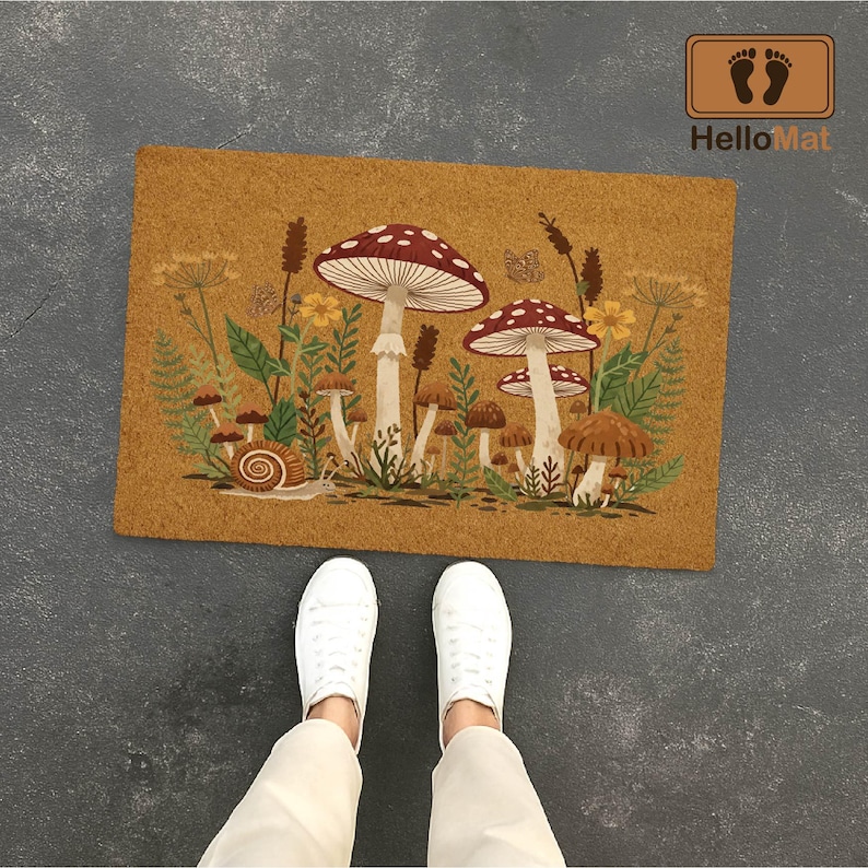 Puede incluir: Una alfombra rectangular con un dise&ntilde;o de setas. La alfombra presenta un fondo marr&oacute;n con una colorida ilustraci&oacute;n de setas, plantas y un caracol. La alfombra tiene el texto "HelloMat" en la esquina superior derecha.