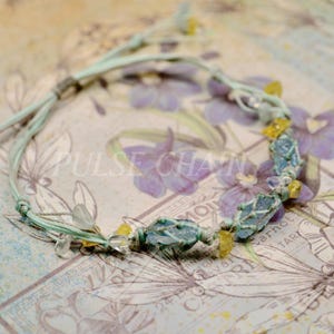 May include: A handmade bracelet featuring light blue and yellow gemstones, strung on a light green cord. The bracelet has a macrame design and the text "PULSE CHAIN" is visible.