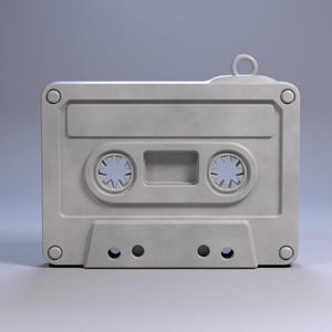 May include: A light grey cassette tape with a loop at the top. The cassette has two circular holes with a star-like design inside. The tape has a rectangular shape with rounded corners and several small holes at the bottom.