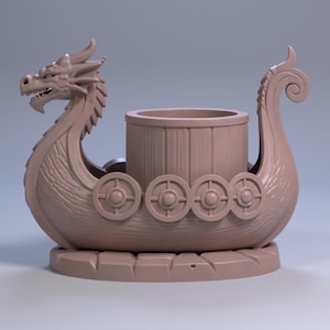 May include: A light brown, 3D-printed Viking ship with a dragon head at the front and a curled stern. The ship features round shields along the sides and a cylindrical container in the centre, suitable for holding small items.