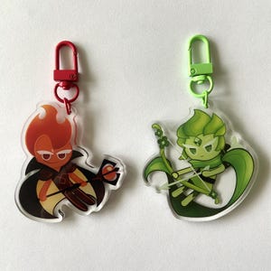 May include: Two acrylic keychains featuring cartoon characters. One keychain has a red clip and depicts a character with orange flames and a black cape. The other has a green clip and shows a green character with a bow and arrow.