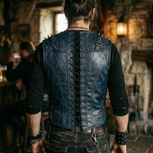 May include: A blue leather vest with a lace-up back and studded accents. The vest has a V-neck and is worn over a black long-sleeved shirt. The vest is part of a gothic or biker-inspired fashion ensemble.