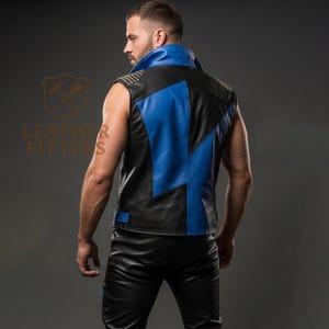 Może przedstawiać: Czarna i niebieska sk&oacute;rzana kamizelka ze srebrnymi ćwiekami na ramionach. Kamizelka ma niebieski kołnierz i geometryczny wz&oacute;r. Logo Leather Fitters jest widoczne w tle.