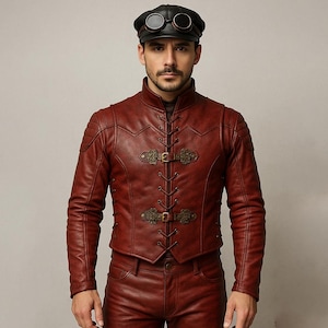 Puede incluir: Chaqueta de cuero burdeos con cierres decorativos de latón y pantalones a juego. La chaqueta presenta un cuello alto y detalles de costura intrincados. La persona de la imagen también lleva una gorra negra con gafas.