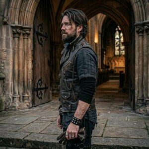 May include: A brown leather vest with metal studs and a chain detail, worn over a dark blue shirt. The vest has a distressed look. The person is wearing a black wristband with studs and holding gloves. The background is a stone building.