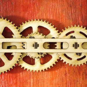 May include: Wooden gears interlocked with a wooden bar, set against a red background. The gears have a light wood color with red accents, and the bar has cut-out sections. A decorative, mechanical-themed item.