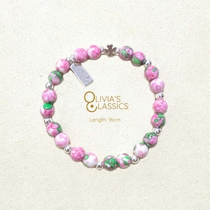 May include: A beaded bracelet featuring pink and green patterned beads, silver spacers, and a small silver charm. The bracelet is 16cm long. The bracelet has the text "Olivia's Classics".