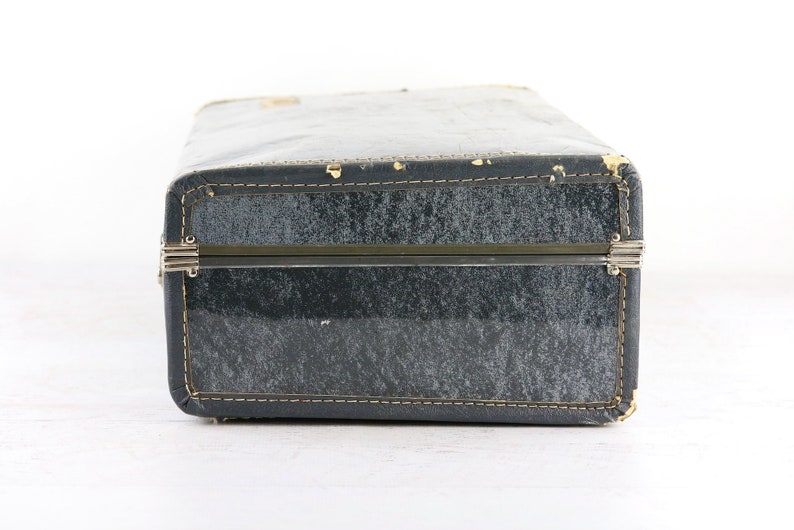 Op de afbeelding: Een vintage blauwe koffer met metalen sluitingen en stiksels rond de randen.