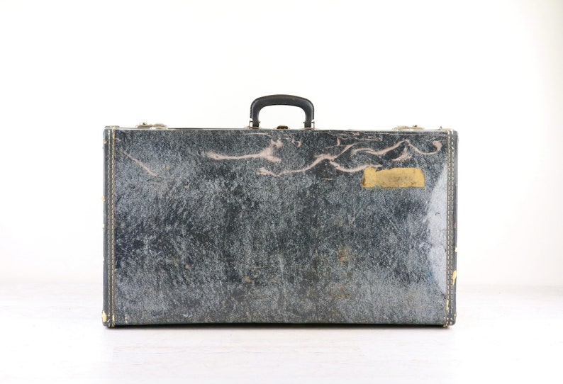 Op de afbeelding: Een vintage zwarte koffer met een versleten leren buitenkant en een messing naamplaatje.