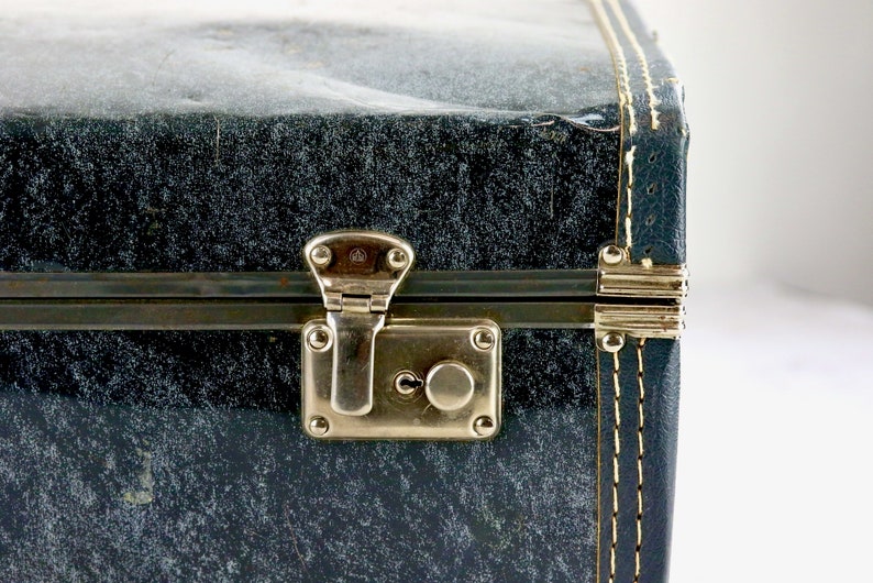 Op de afbeelding: Close-up van een blauwe vintage koffer met een messing slot en een gouden rand. De koffer heeft een gestikte naad langs de rand.