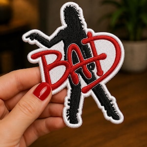 May include: Embroidered patch featuring a black silhouette of a person with the word "BAD" in red, outlined in white. The patch has a white border and is designed for application on clothing or accessories.