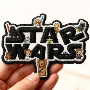 Op de afbeelding: Geborduurde patch met de woorden "STAR WARS" in zwart, omlijnd met wit. De patch bevat cartoon illustraties van personages zoals Darth Vader, Yoda en Chewbacca. De patch wordt door een hand vastgehouden.