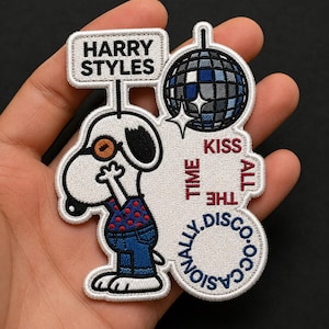 Op de afbeelding: Geborduurde patch met een cartoonhond met een bril en een rood polkadotshirt, met de tekst "HARRY STYLES" en "TIME ALL THE DISCO.CASIONALLY. KISS". De patch bevat een discobal.