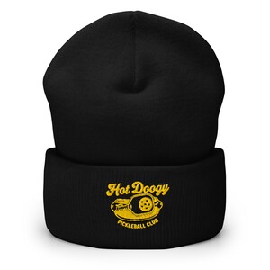May include: Black beanie with the text "Hot Doogy Pickleball Club" embroidered in yellow. The design includes a pickleball paddle and ball. The beanie is a warm, comfortable accessory for pickleball enthusiasts.