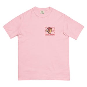 May include: A light pink t-shirt featuring a cartoon hot dog character with a pink bow and the text "Hello Doogy." The graphic is on the left chest area. The shirt has a crew neck and short sleeves.