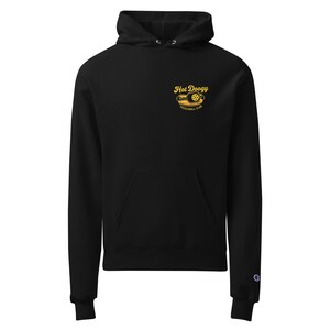 May include: Black hoodie with a front pocket and drawstring hood. The hoodie features a yellow graphic on the upper left chest that reads "Hot Doogy Pickleball Club". The Champion logo is on the left sleeve.