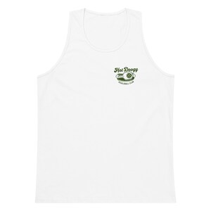 May include: White tank top with a green graphic that reads "Hot Doogy Pickleball Club". The graphic features a pickleball and a paddle. The tank top is sleeveless with a scoop neck.