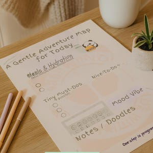 May include: A printable daily planner with sections for meals, hydration, and notes, alongside a panda illustration. A cup of tea and a small plant sit nearby. Pastel colored pens are on the table.