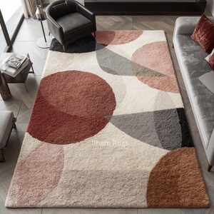 May include: A large rectangular rug with a geometric design. The rug features overlapping circles and shapes in shades of red, pink, grey, and beige against a cream background. The text "Ilham Rugs" is visible on the rug.