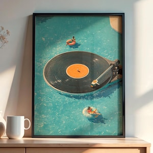 May include: A framed print shows a record player in a swimming pool with two people on inflatable rings. The artwork is in a black frame, displayed on a wooden cabinet with white vases and a mug.