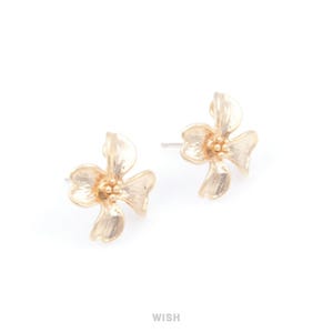 May include: A pair of gold-colored flower stud earrings. Each earring features a detailed floral design with multiple petals and a textured surface. The earrings are set against a white background.