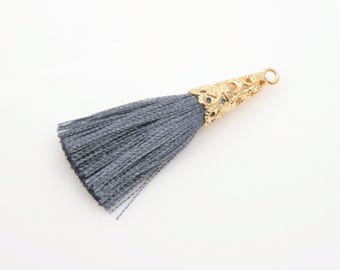 May include: A gray tassel with a gold-colored filigree cone-shaped cap and a small loop at the top. The tassel is made of many strands of gray thread. The word "WISH" is printed in the bottom center of the image.