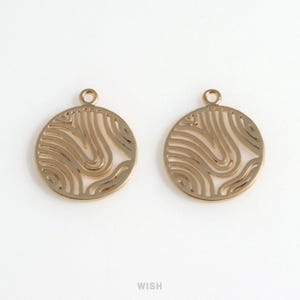 May include: Two gold-colored, round pendants with a cut-out, wave-like design. Each pendant has a small loop at the top for attaching to a chain or other jewelry component. The pendants are displayed on a white background.