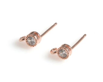 Puede incluir: Un par de pendientes de botón de oro rosa con una gema redonda y transparente. Los pendientes tienen un delicado engaste festoneado y un poste para orejas perforadas. La palabra "WISH" está impresa en la parte inferior de la imagen.