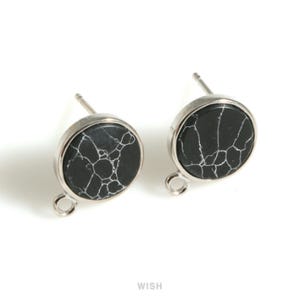 Könnte beinhalten: Ein Paar runde Ohrstecker mit einem schwarz-weißen Marmormuster. Die Ohrringe haben eine silberfarbene Metalleinfassung und einen Stecker für durchbohrte Ohren. Sie haben eine kleine Schlaufe unten.