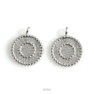 Könnte beinhalten: Zwei silberfarbene ovale Anhänger mit einem strukturierten, gepunkteten Design. Jeder Anhänger hat oben eine kleine Schlaufe zum Befestigen an einer Kette oder einem anderen Schmuckbestandteil. Das Wort "WISH" ist unten aufgedruckt.