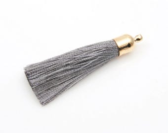 May include: A gray tassel with a gold-colored cap. The tassel is made of many strands of gray thread. The gold cap has a small loop at the top. The tassel is on a white background.