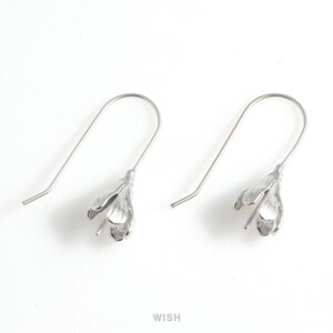 May include: A pair of silver-colored flower-shaped dangle earrings. Each earring features a delicate floral design with three petals and a curved hook for the ear. The earrings are displayed against a white background.