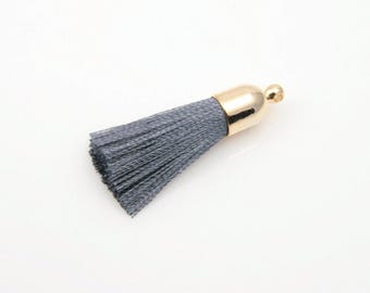 May include: A single gray tassel with a gold-colored cap and loop. The tassel is made of tightly packed threads, and the cap has a smooth, shiny finish. The tassel is set against a white background.
