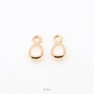 Puede incluir: Dos colgantes de joyería dorados en forma de lágrima con un lazo en la parte superior. Los colgantes son lisos y brillantes, sobre un fondo blanco. La palabra "WISH" está impresa en el centro inferior.