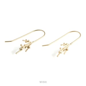 May include: A pair of gold-colored, branch-shaped earrings. Each earring features a long, curved hook and a detailed branch design with small, textured elements. The word "WISH" is printed in the bottom center.