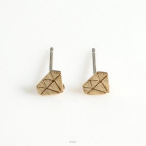 May include: A pair of gold-colored stud earrings. Each earring is shaped like a geometric diamond with etched lines. The earrings have a post backing for pierced ears. The background is white.