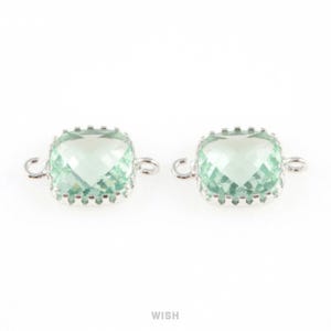 Può includere: Due connettori di gemme quadrati verde chiaro con montature in metallo argentato. Ogni gemma ha una superficie sfaccettata e un anello su ogni lato per il fissaggio. La parola "WISH" è in basso.