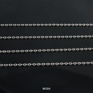 Puede incluir: Primer plano de cuatro collares de cadena plateados sobre un fondo negro. Las cadenas están hechas de pequeños eslabones espaciados uniformemente. La palabra "WISH" está impresa en blanco en la parte inferior de la imagen.