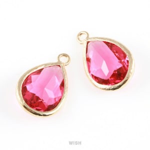 May include: Two teardrop-shaped pendants with faceted pink gemstones set in gold-coloured bezels. Each pendant has a small loop at the top for attaching to a chain or other jewellery component. The background is white.