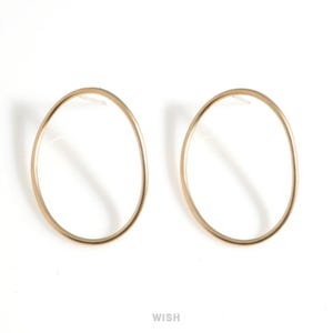 Può includere: Un paio di orecchini a cerchio ovali color oro. Gli orecchini hanno un design semplice con una finitura liscia e lucida. Gli orecchini sono su uno sfondo bianco.
