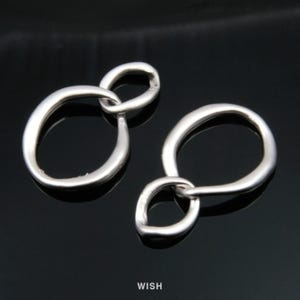May include: Two silver-toned, abstract charm pendants. Each pendant features two interconnected, rounded loops. The pendants are displayed against a black background. The word "WISH" is printed in white at the bottom of the image.
