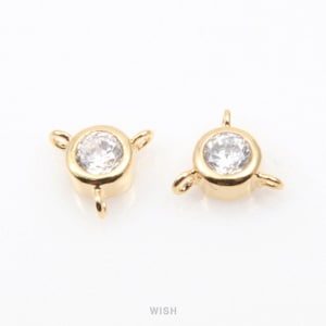 May include: Two gold-colored jewelry findings, each featuring a clear, round gemstone set in a bezel. Each finding has three small loops for attachment. The findings are displayed on a white background.