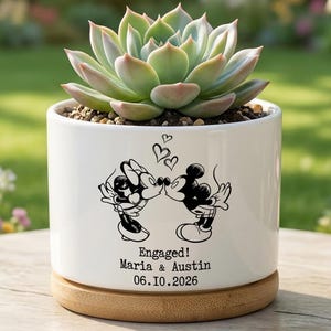 May include: A white ceramic cylindrical planter with a bamboo base containing a green succulent. The planter features a black graphic of two cartoon mice kissing with hearts above them and the text "Engaged! Maria & Austin 06.10.2026".